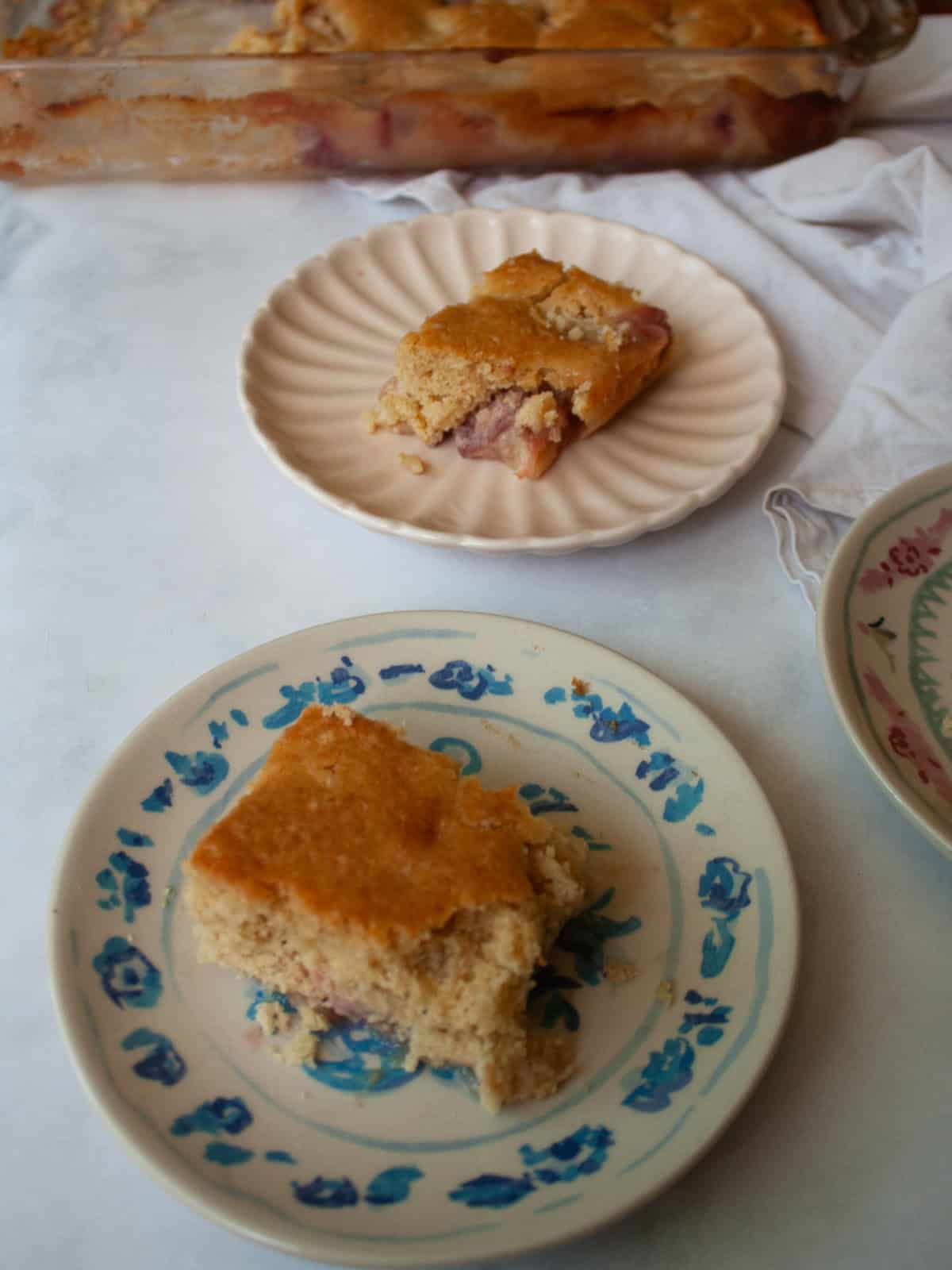This gluten free peach cobbler features juicy peaches tucked into a pillowy gluten-free batter to make a rustic, simple dessert. Two plates of gluten free peach cobbler near a pan of cobbler.