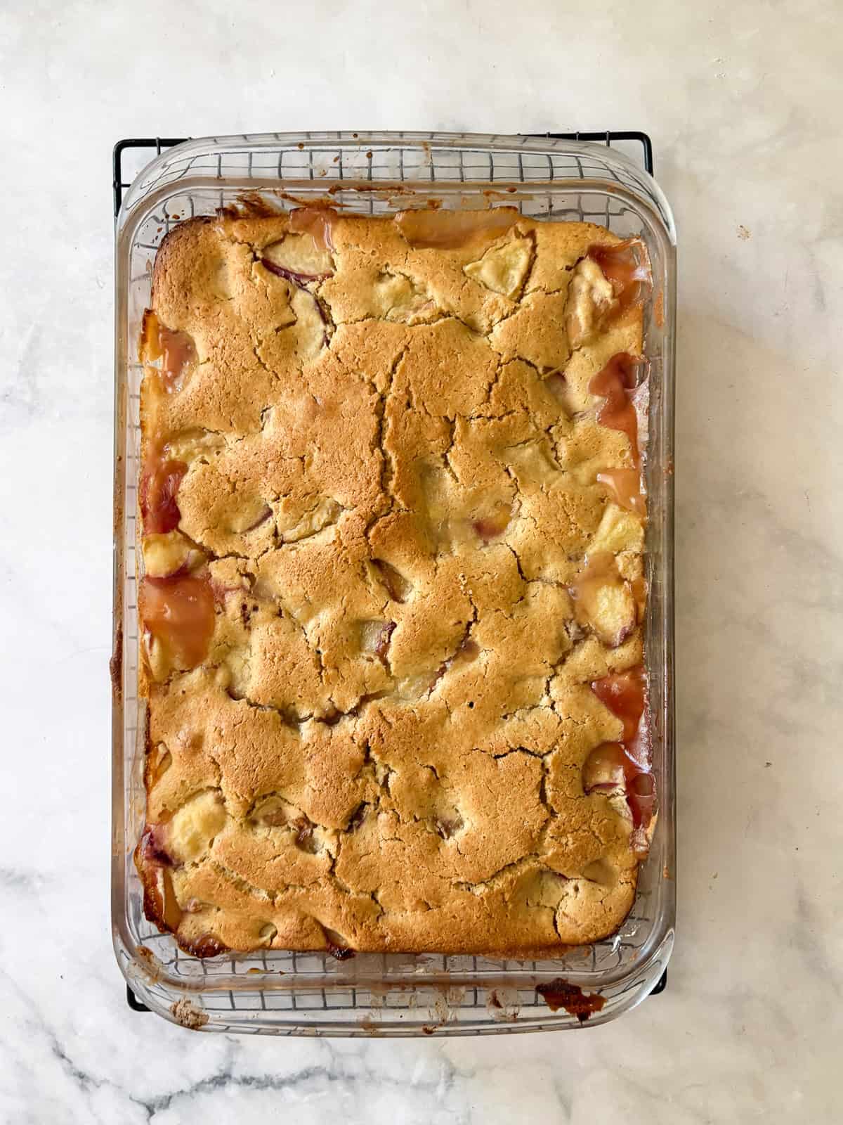 This gluten free peach cobbler features juicy peaches tucked into a pillowy gluten-free batter to make a rustic, simple dessert. A pan of baked gluten free peach cobberl.