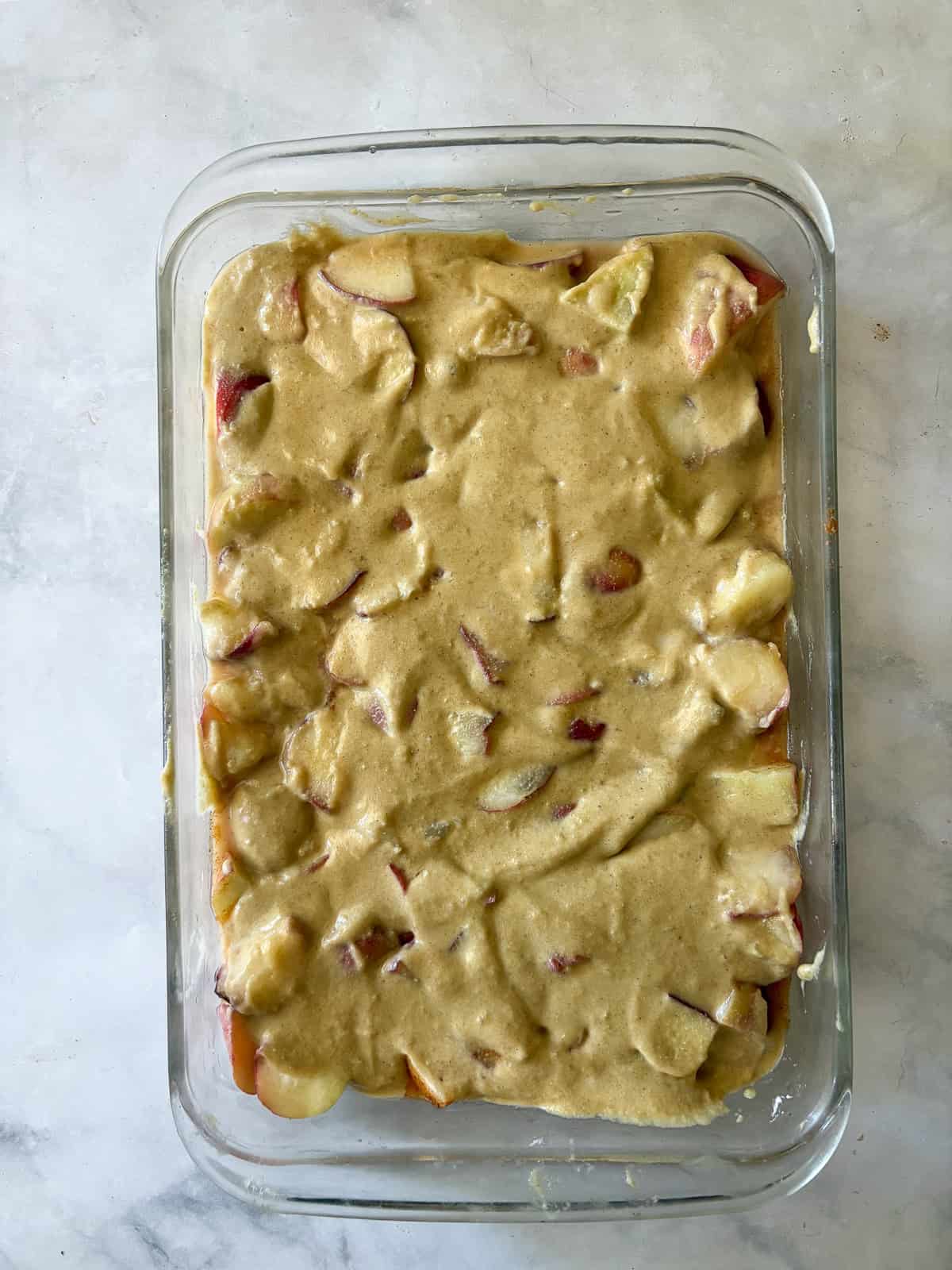 This gluten free peach cobbler features juicy peaches tucked into a pillowy gluten-free batter to make a rustic, simple dessert. Cobbler topping spread over a pan of gluten free peach cobbler.