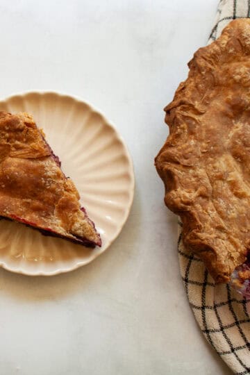 A piece of piece with a whole wheat crust on a plate next to a pie.