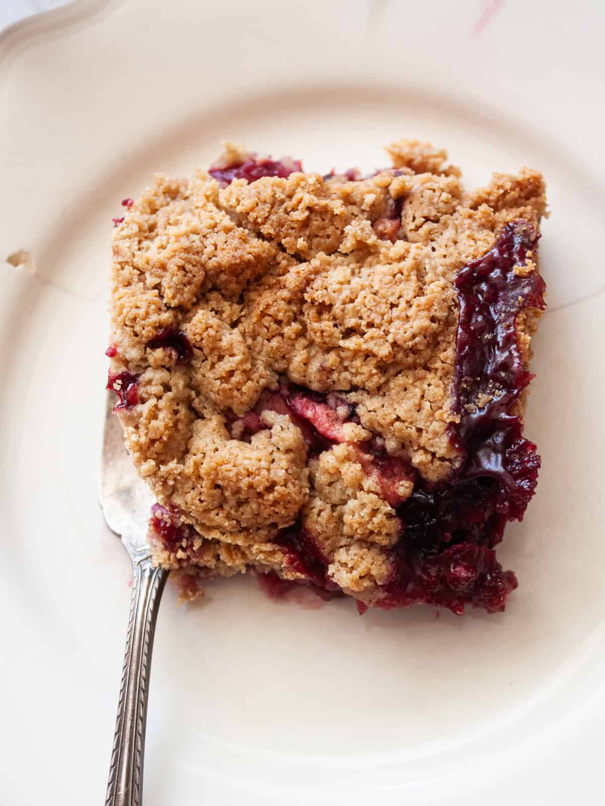 This delicious apple blackberry crumble stars juicy pockets of berries, sweet-tart apples, cinnamon, brown sugar, and a buttery topping. A fork rests next to a slice of apple blackberry crumble on a plate.