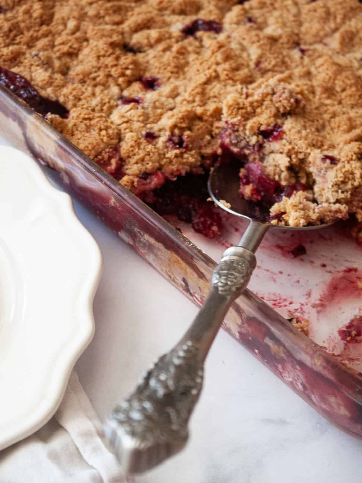 This delicious apple blackberry crumble stars juicy pockets of berries, sweet-tart apples, cinnamon, brown sugar, and a buttery topping. A serving spoon in a pan of apple blackberry crumble.