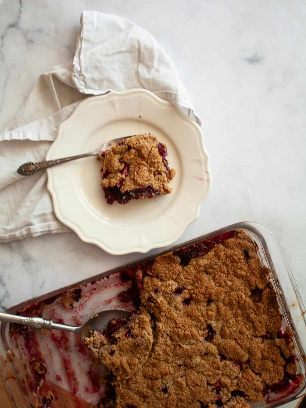 A pan of apple blackberry crumble next to a piece of crumble on a plate.