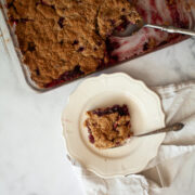 A pan of apple blackberry crumble next to a piece of crumble on a plate.