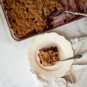 A pan of apple blackberry crumble next to a piece of crumble on a plate.