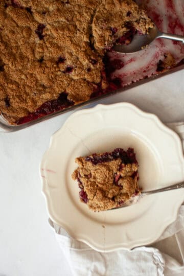 A pan of apple blackberry crumble next to a piece of crumble on a plate.