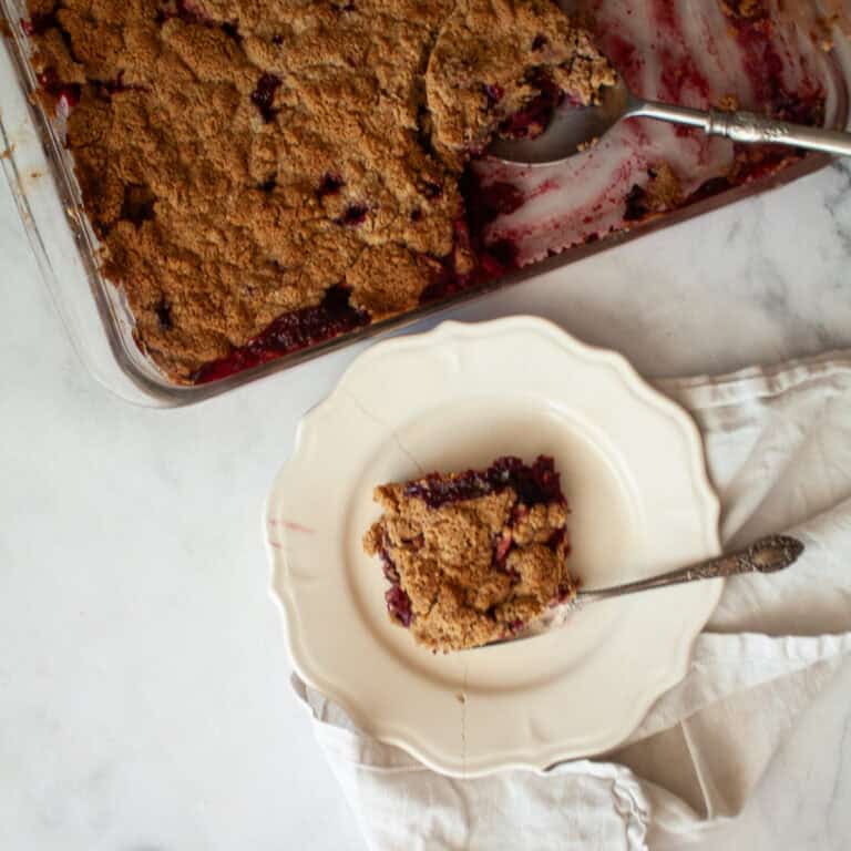 A pan of apple blackberry crumble next to a piece of crumble on a plate.