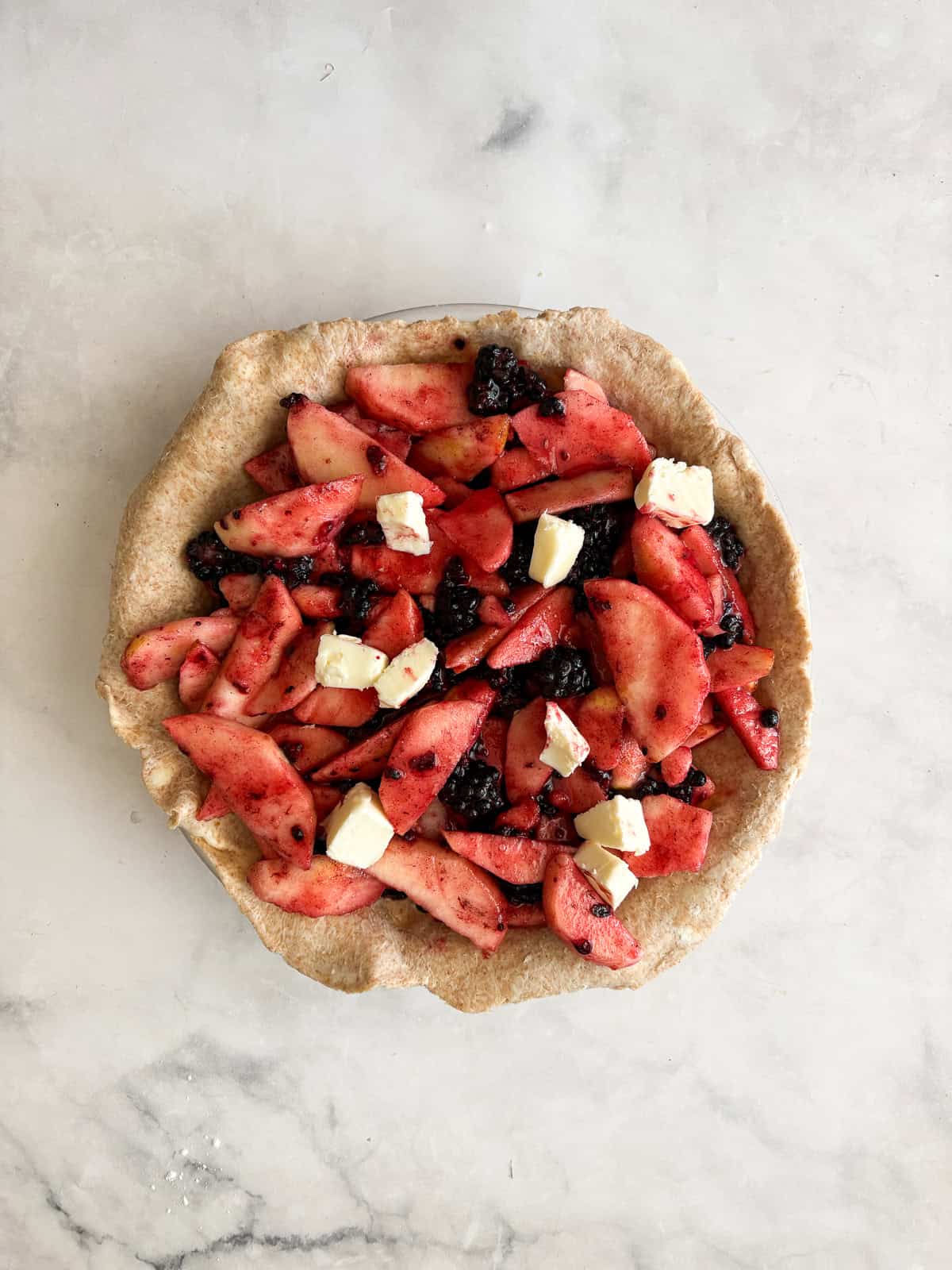 Juicy apples combine with sun-warmed blackberries in this apple blackberry pie. Choose a homemade, gluten-free, or store-bought pie crust. Apple blackberry pie filling is topped with butter in a pie plate.