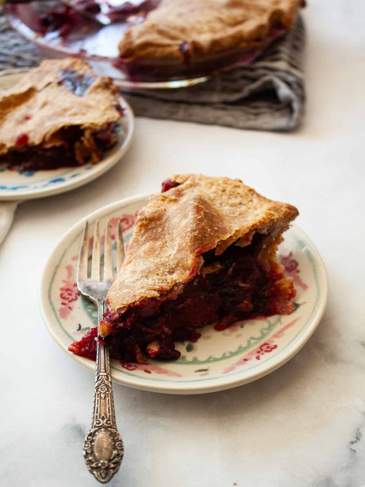 Juicy apples combine with sun-warmed blackberries in this apple blackberry pie. Choose a homemade, gluten-free, or store-bought pie crust. A fork rests on a plate next to a slice of apple blackberry pie.