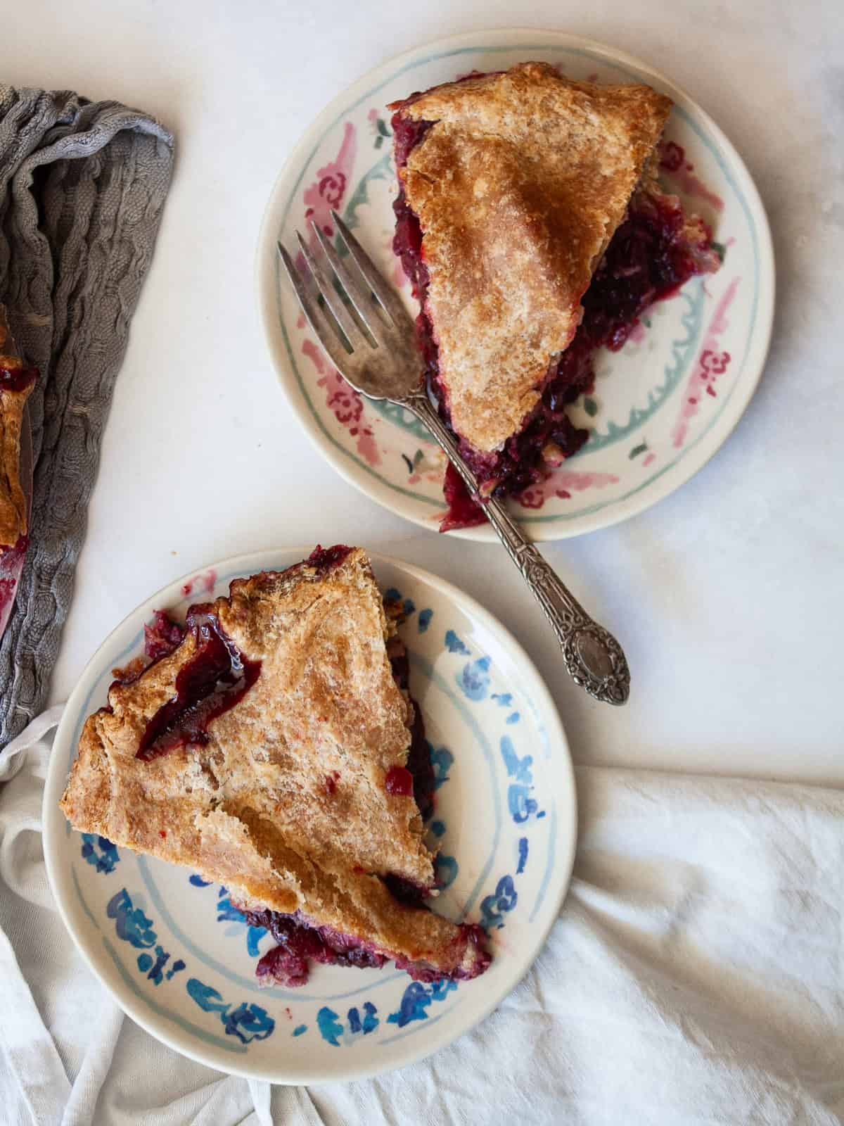 Juicy apples combine with sun-warmed blackberries in this apple blackberry pie. Choose a homemade, gluten-free, or store-bought pie crust. Slices of apple blackberry pie on plates with a napkin next to it.