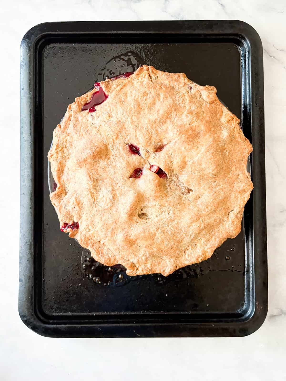 Juicy apples combine with sun-warmed blackberries in this apple blackberry pie. Choose a homemade, gluten-free, or store-bought pie crust. A baked apple blackberry pie on a baking sheet.