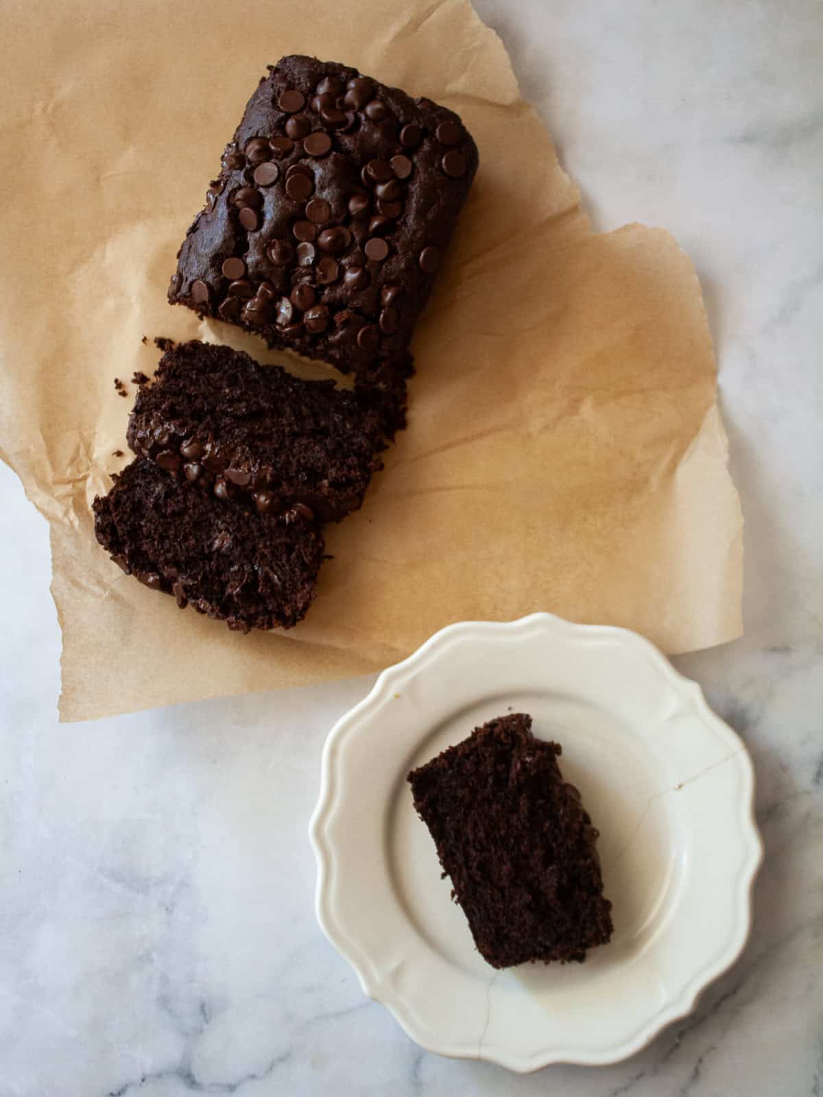 This rich, double chocolate banana bread can be made gluten free or with whole wheat flour for a dense, moist, and utterly delectable loaf. A sliced loaf of double chocolate banana bread on parchment paper and a slice on a plate.