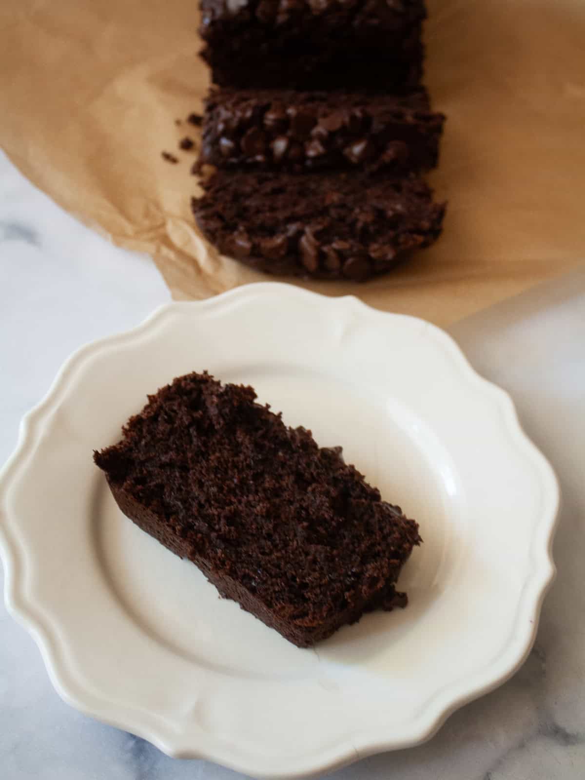 This rich, double chocolate banana bread can be made gluten free or with whole wheat flour for a dense, moist, and utterly delectable loaf. A slice of double chocolate banana bread on a plate next to the laof.