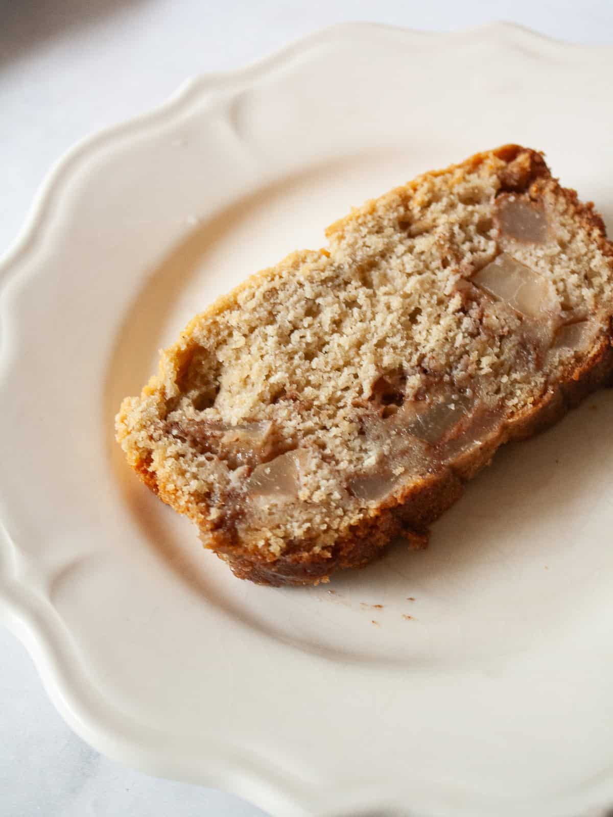 This one-bowl pear bread is a lovely sweet nibble, with a cozy mix of cinnamon and brown sugar-laced chopped pears in a whole grain loaf. A slice of pear bread on a plate.