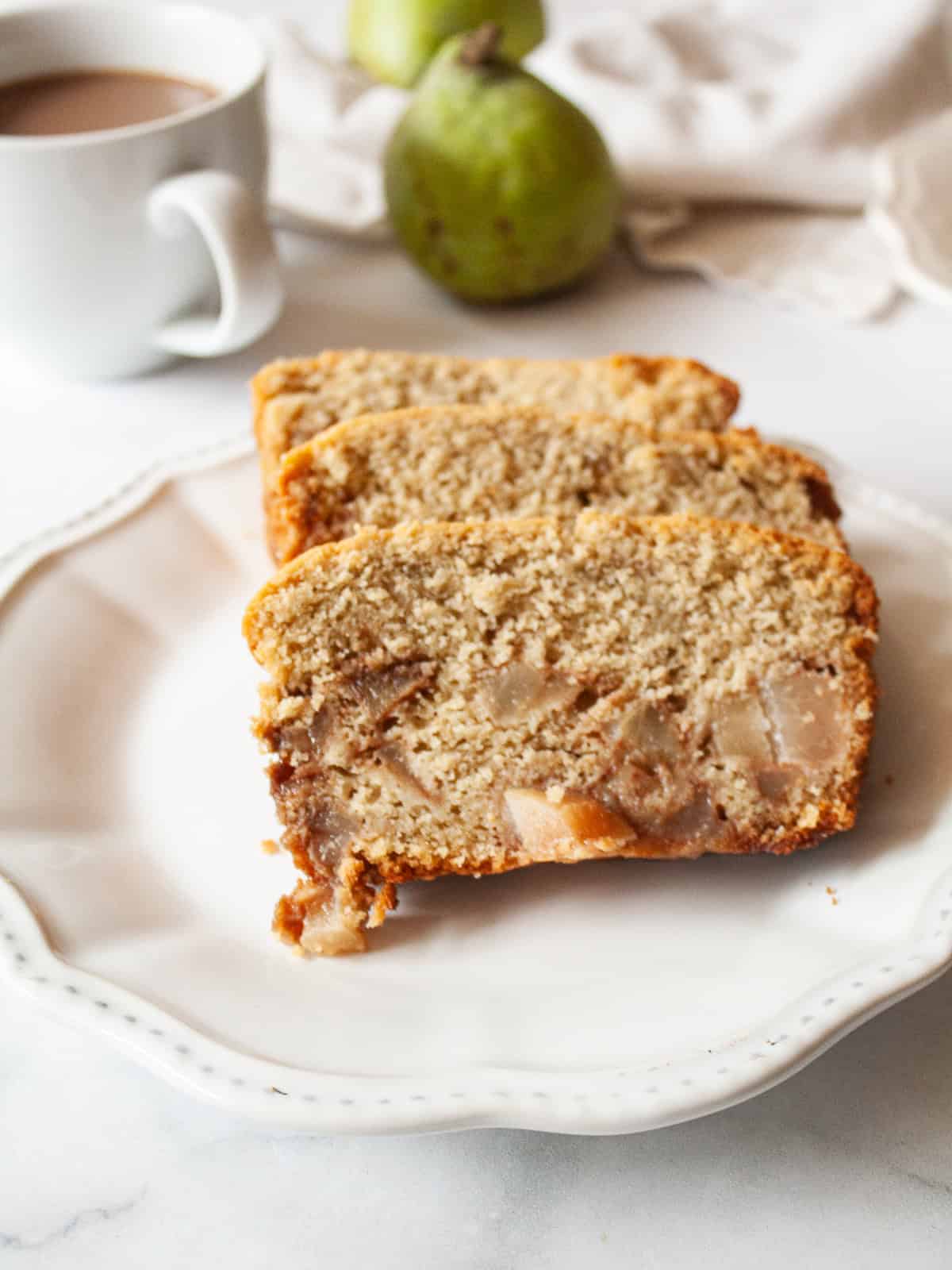 Slices of pear bread on a plate with a pear behind them.