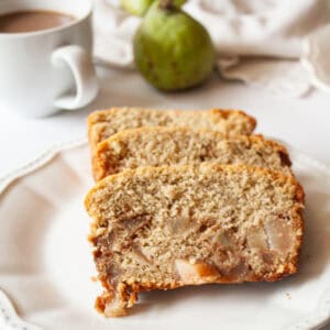Slices of pear bread on a plate with a pear behind them.