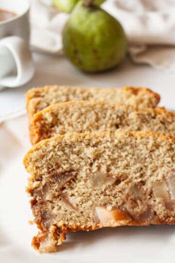 Slices of pear bread on a plate with a pear behind them.