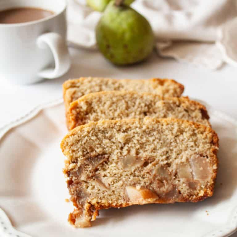 Slices of pear bread on a plate with a pear behind them.