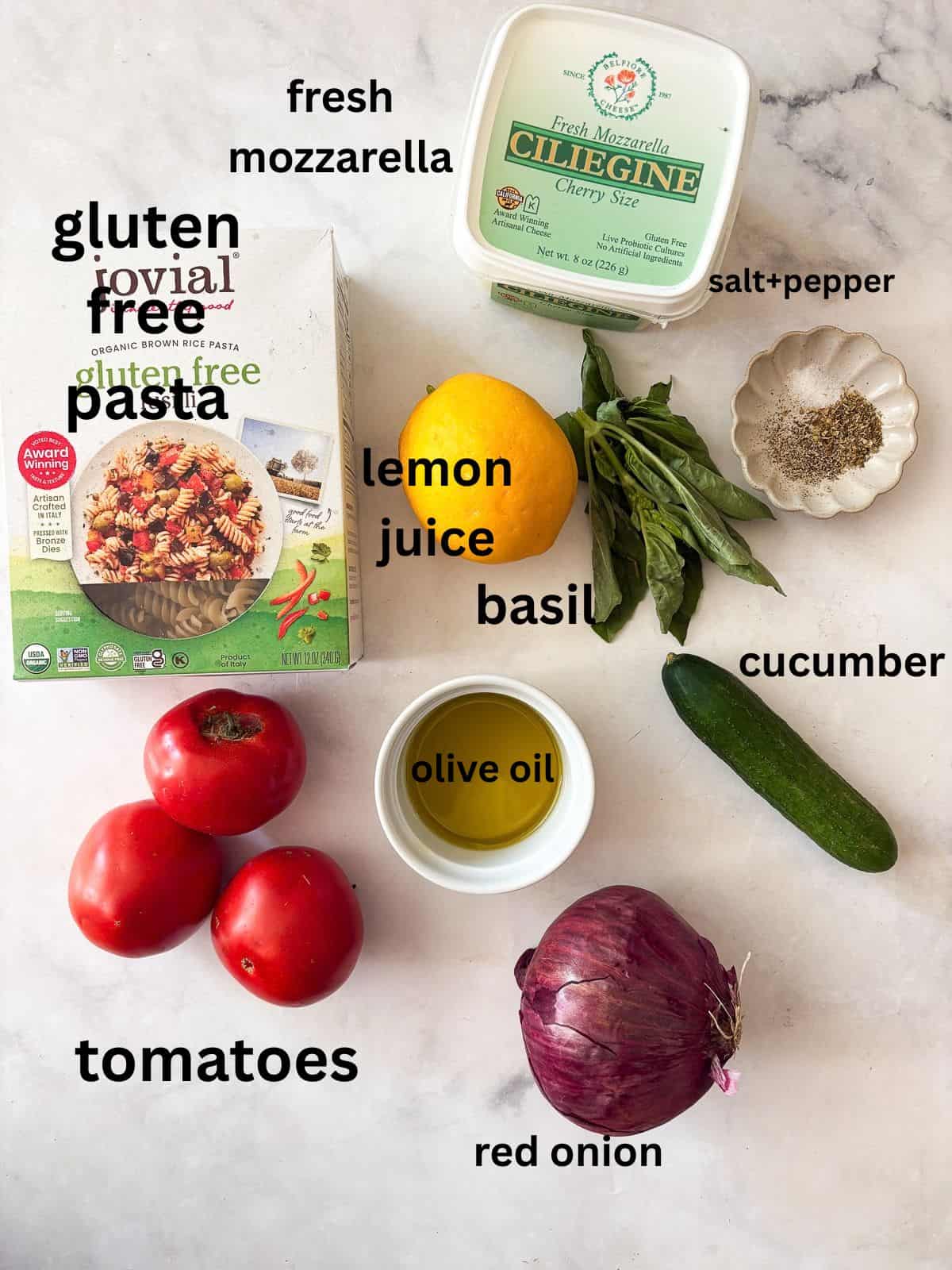 A summer staple, my gluten free pasta salad recipe features a zingy lemon dressing, fresh mozzarella, tomatoes, and fresh herbs. Ingredients for gluten free pasta salad are text-labeled.