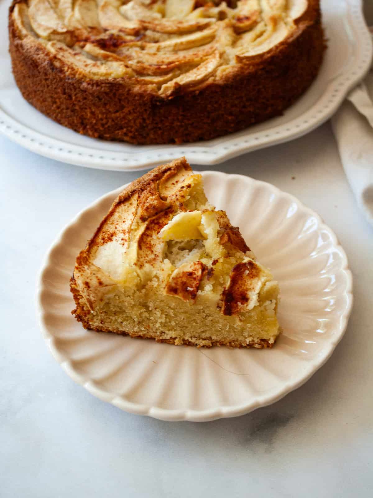 This rich-tasting almond flour apple cake has a wonderfully moist and tender crumb that's topped with sliced apples and maple syrup. A side view of a slice of almond flour apple cake.