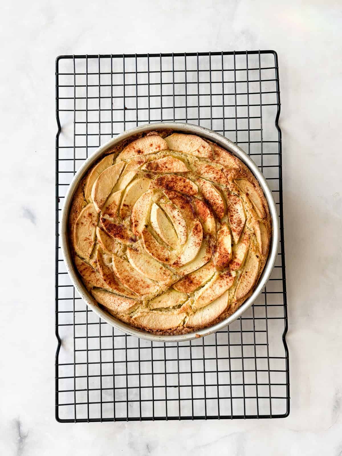 This rich-tasting almond flour apple cake has a wonderfully moist and tender crumb that's topped with sliced apples and maple syrup. A baked almond flour apple cake cools in a pan.