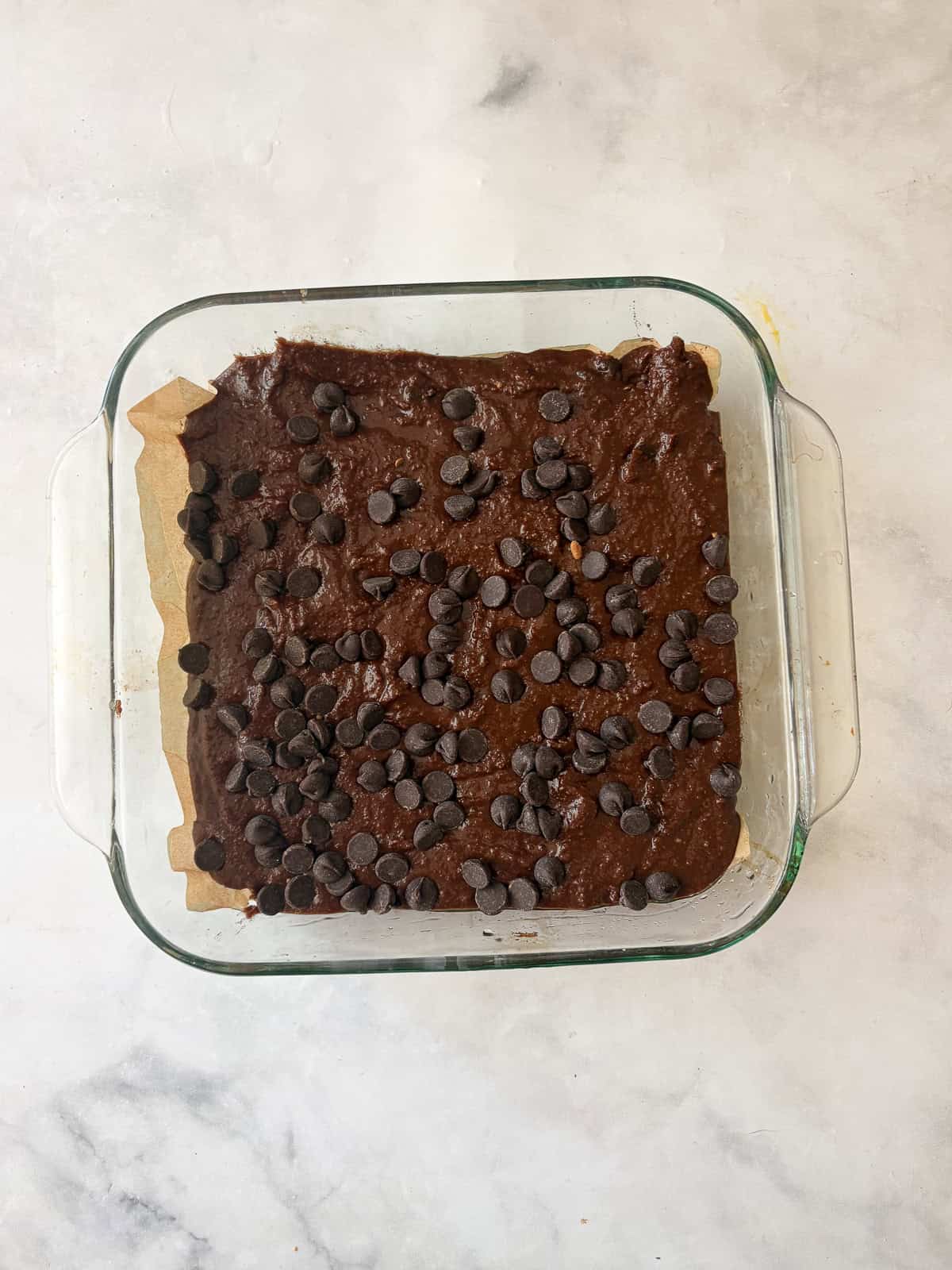 This irresistible one bowl almond flour chocolate cake is wonderfully fluffy and rich, and you need just one simple flour to make it. Chocolate chips are sprinkled over almond flour chocolate cake batter in a pan.