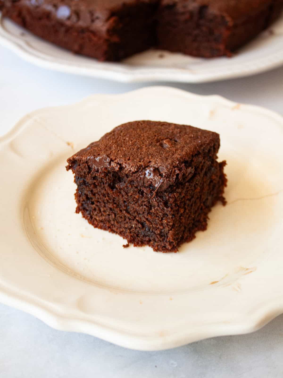 This irresistible one bowl almond flour chocolate cake is wonderfully fluffy and rich, and you need just one simple flour to make it. A slice of almond flour chocolate cake on a plate with the cake behind it.