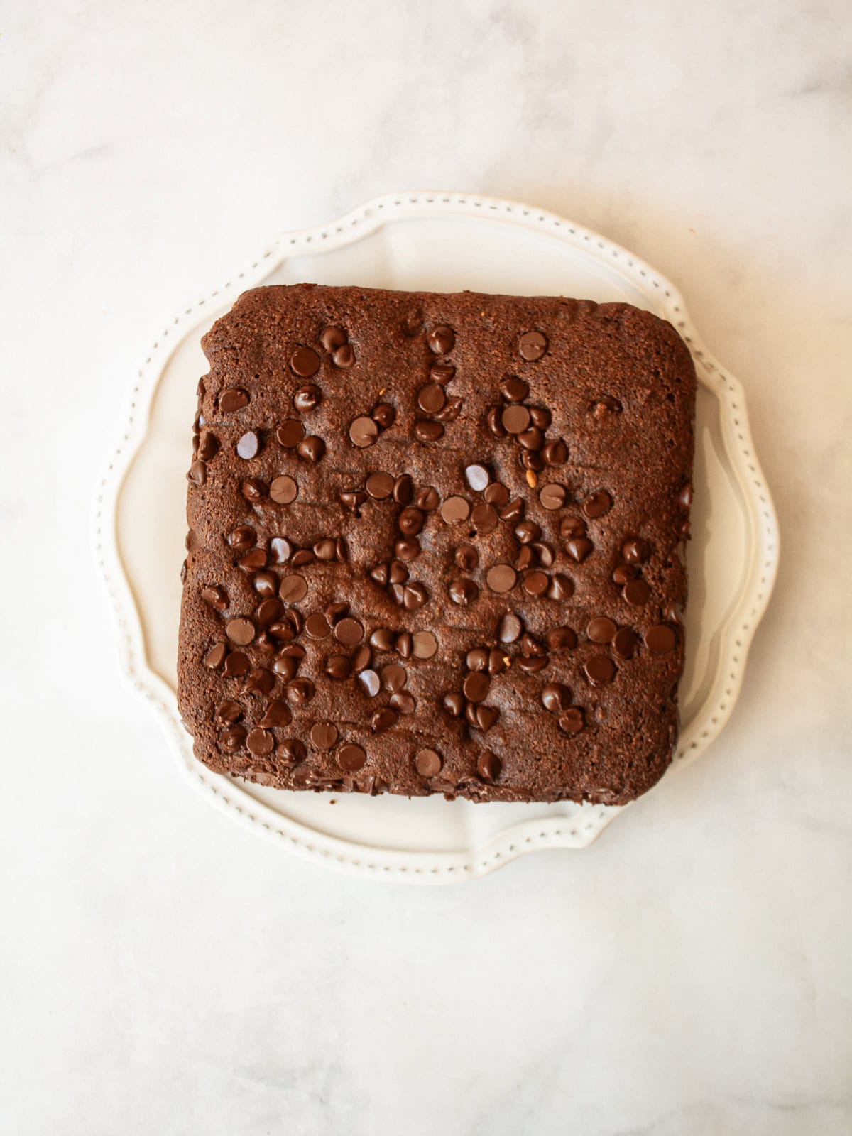 This irresistible one bowl almond flour chocolate cake is wonderfully fluffy and rich, and you need just one simple flour to make it. Chocolate chips are seen on the top of an almond flour chocolate cake on a plate.