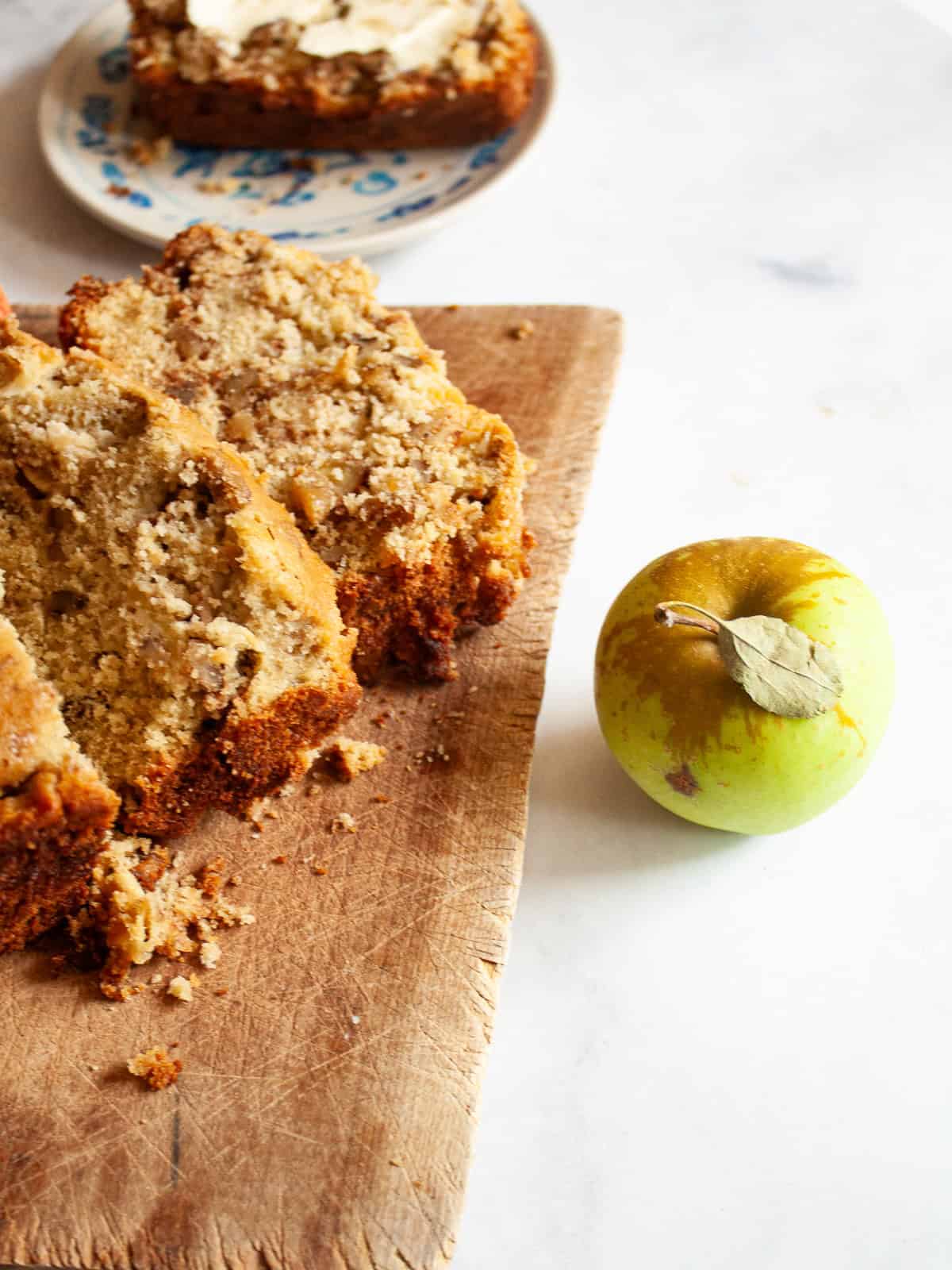 This easy apple walnut bread is tender and filled with fresh apples and crunchy walnuts. Make it with whole wheat flour or oat flour. A green apple next to a cutting board with slices of apple walnut bread.