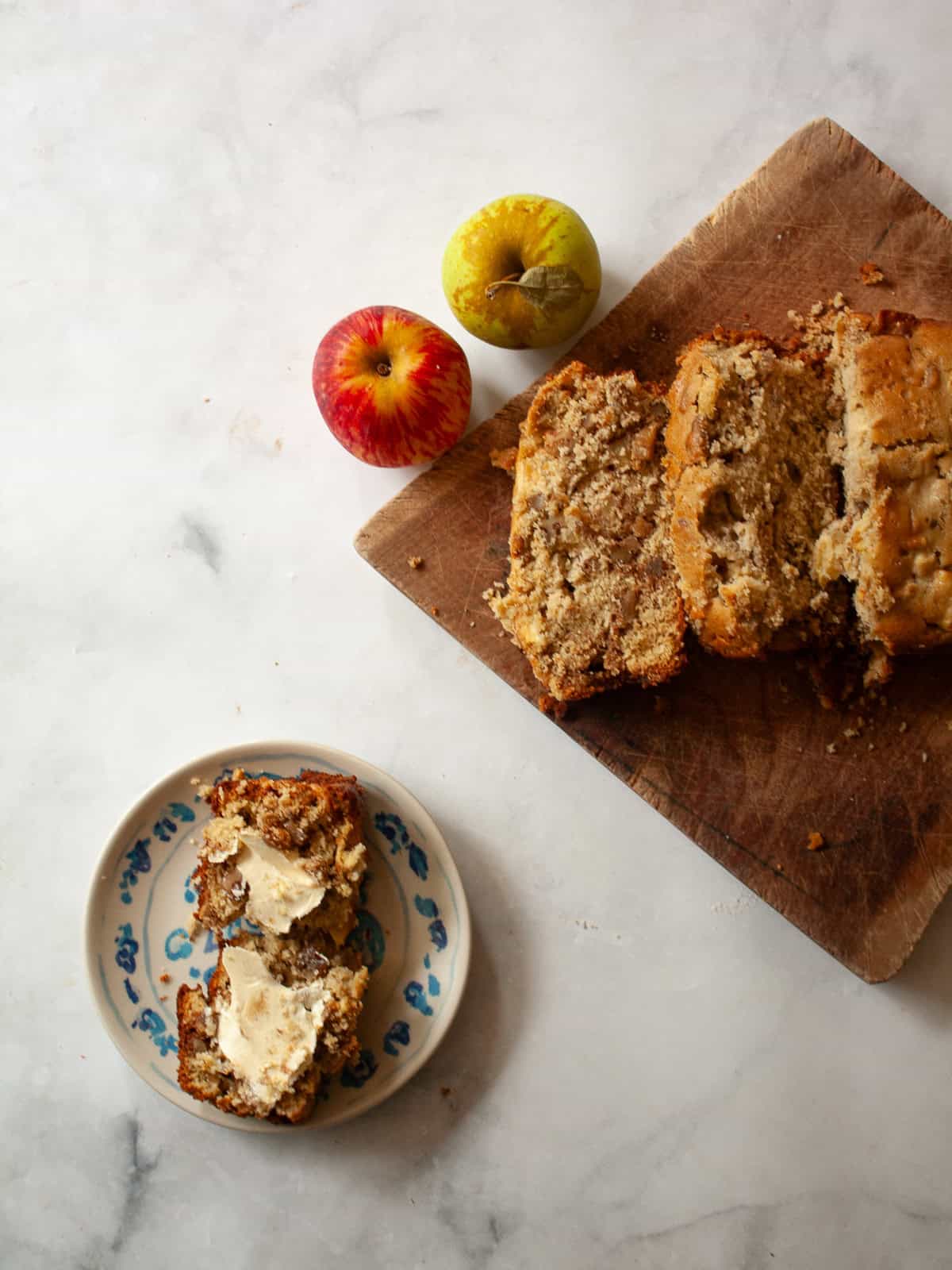 This easy apple walnut bread is tender and filled with fresh apples and crunchy walnuts. Make it with whole wheat flour or oat flour. A buttered slice of apple walnut bread on a plate next to a sliced loaf and two apples.