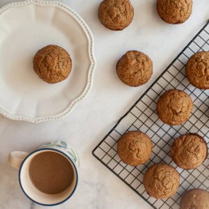 A rack of applesauce muffins, a muffin on a plate, and a cup of coffee.