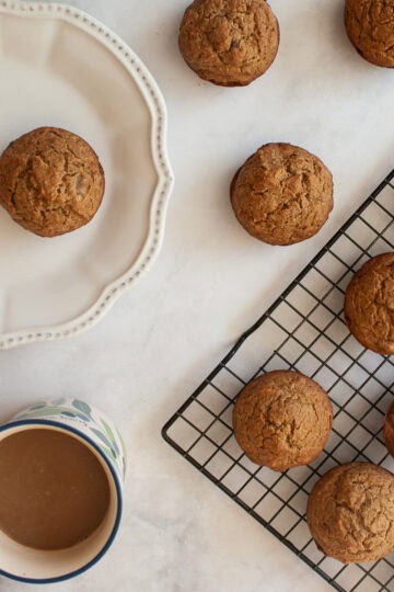A rack of applesauce muffins, a muffin on a plate, and a cup of coffee.