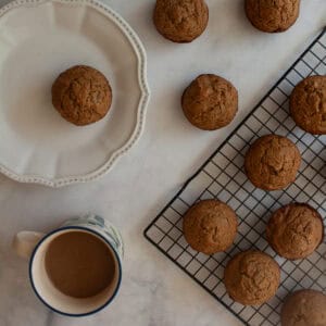 A rack of applesauce muffins, a muffin on a plate, and a cup of coffee.