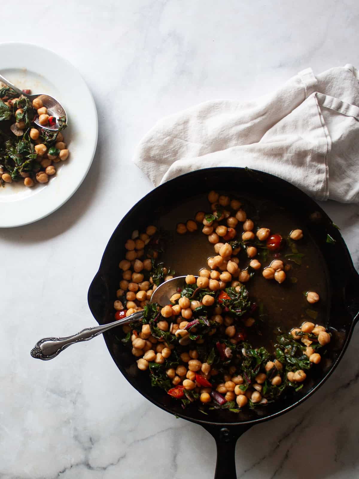 This easy beans and greens recipe comes together in minutes with pantry beans and fresh greens. A simple, adaptable weeknight meal. A cast iron skillet of beans and greens and a plate of beans and greens.