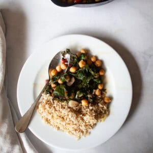A spoon rests alongside a serving of beans and greens on a plate.