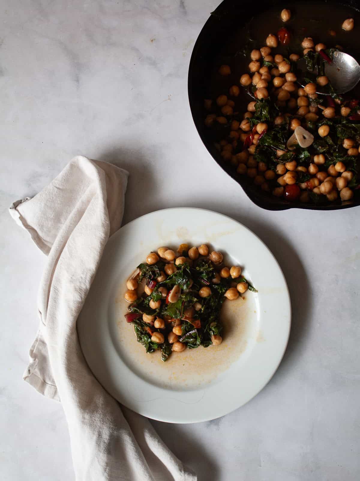 This easy beans and greens recipe comes together in minutes with pantry beans and fresh greens. A simple, adaptable weeknight meal. A plate of beans and greens with a napkin and the pan next to it.