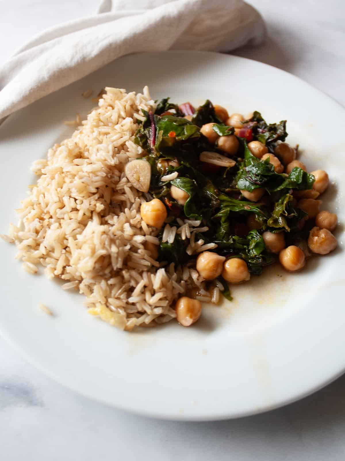 This easy beans and greens recipe comes together in minutes with pantry beans and fresh greens. A simple, adaptable weeknight meal. Brown rice is next to beans and greens on a plate.