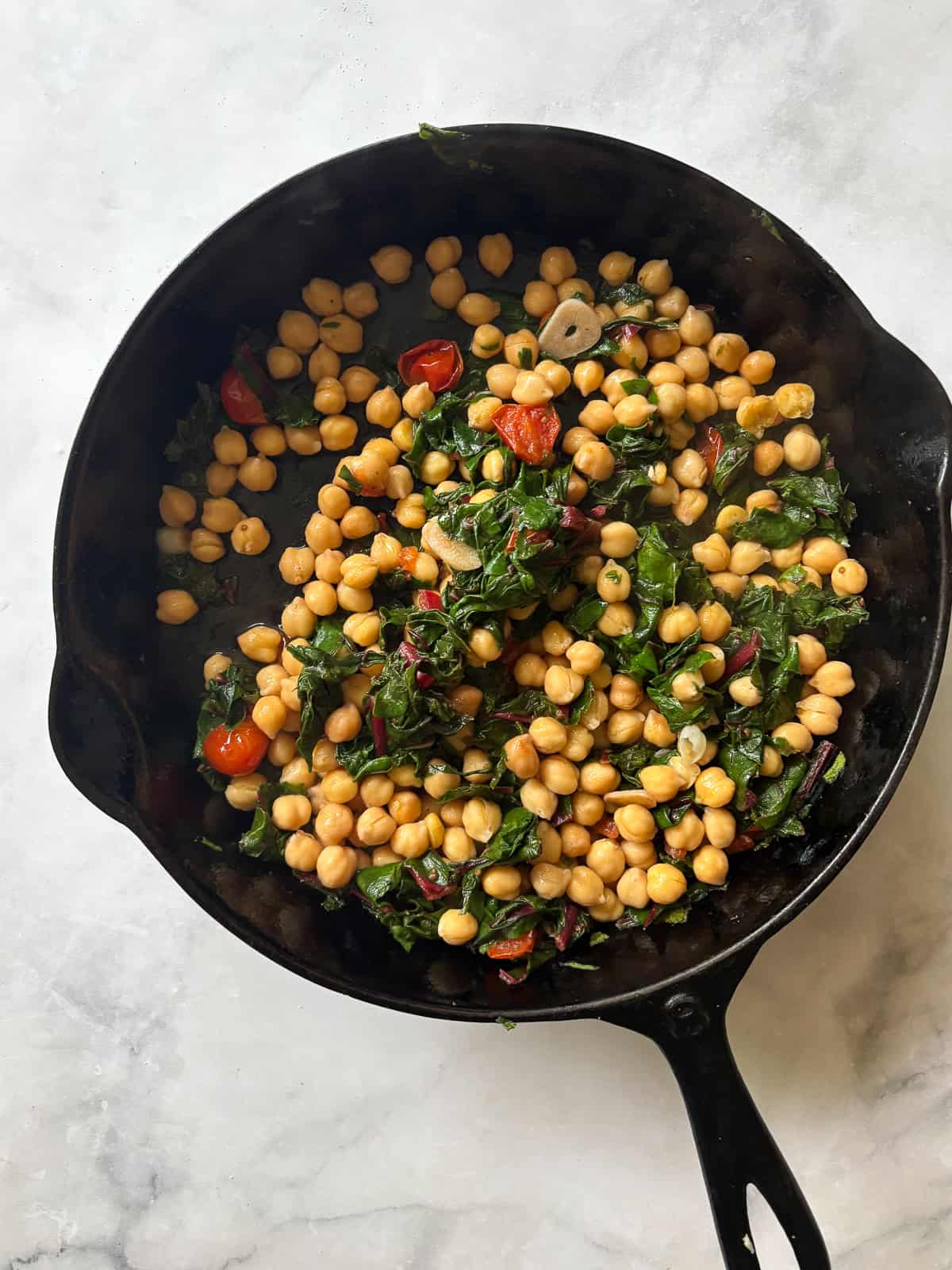 This easy beans and greens recipe comes together in minutes with pantry beans and fresh greens. A simple, adaptable weeknight meal. Chickpeas are added to a skillet for beans and greens.