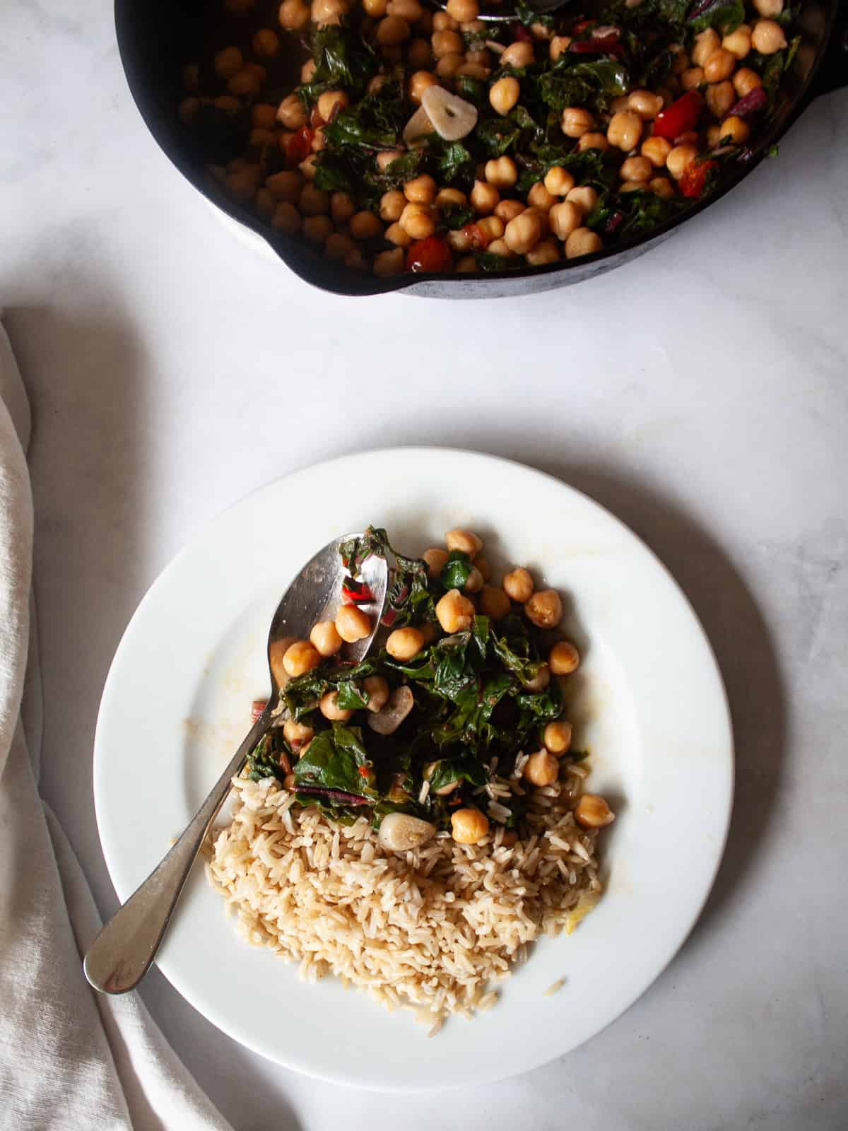This easy beans and greens recipe comes together in minutes with pantry beans and fresh greens. A simple, adaptable weeknight meal. A plate of brown rice and beans and greens and a skillet.