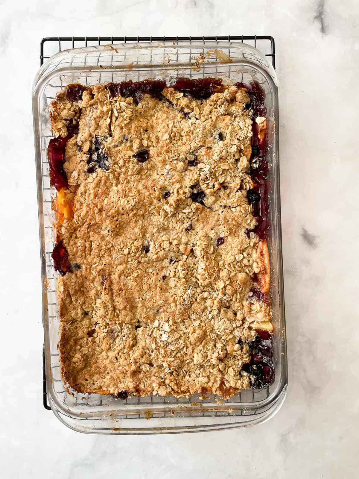 This apple blueberry crisp combines juicy summer apples and berries under a buttery oat topping. A seasonal dessert that's delicious warm. A baked pan of apple blueberry crisp cools on a rack.