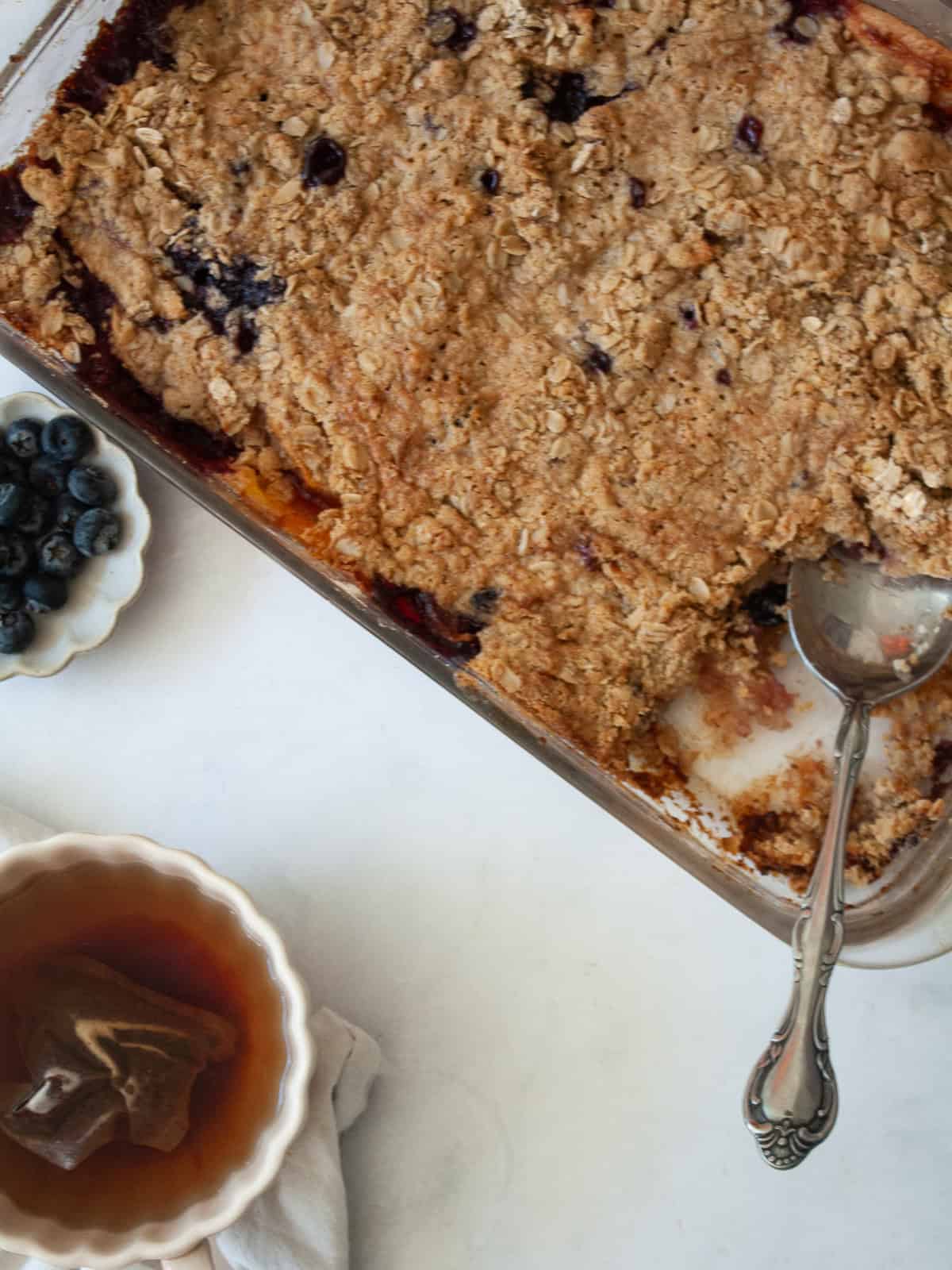 This apple blueberry crisp combines juicy summer apples and berries under a buttery oat topping. A seasonal dessert that's delicious warm. A pan of apple blueberry crisp next to blueberries.