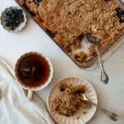 A cup of tea and a portion of apple blueberry crisp and a pan of crisp.