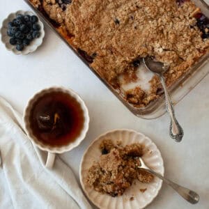 A cup of tea and a portion of apple blueberry crisp and a pan of crisp.