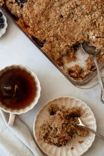 A cup of tea and a portion of apple blueberry crisp and a pan of crisp.