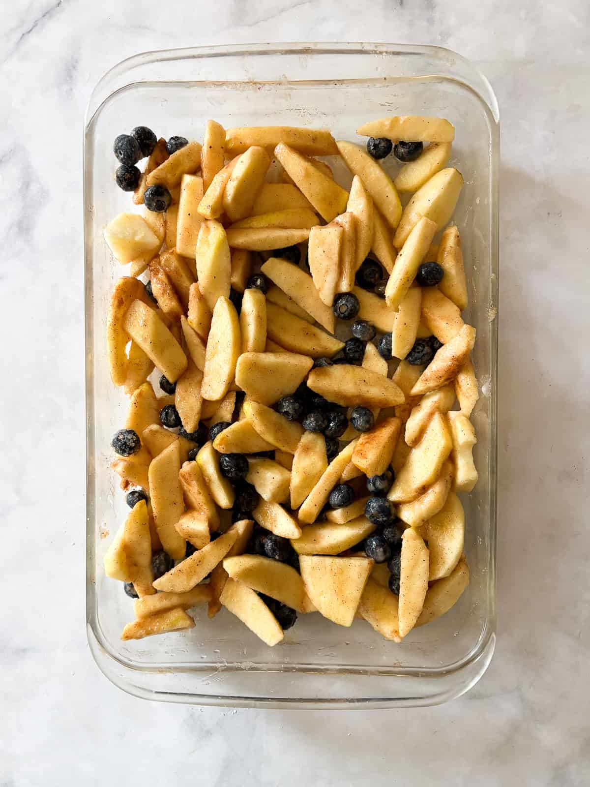 This apple blueberry crisp combines juicy summer apples and berries under a buttery oat topping. A seasonal dessert that's delicious warm. Fruit is mixed in a pan for apple blueberry crisp.