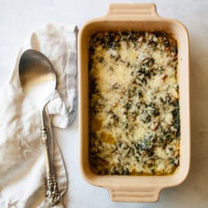A serving spoon rests on a napkin next to a dish of chard gratin.