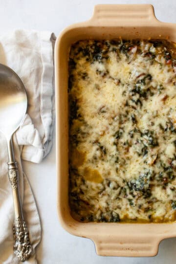 A serving spoon rests on a napkin next to a dish of chard gratin.