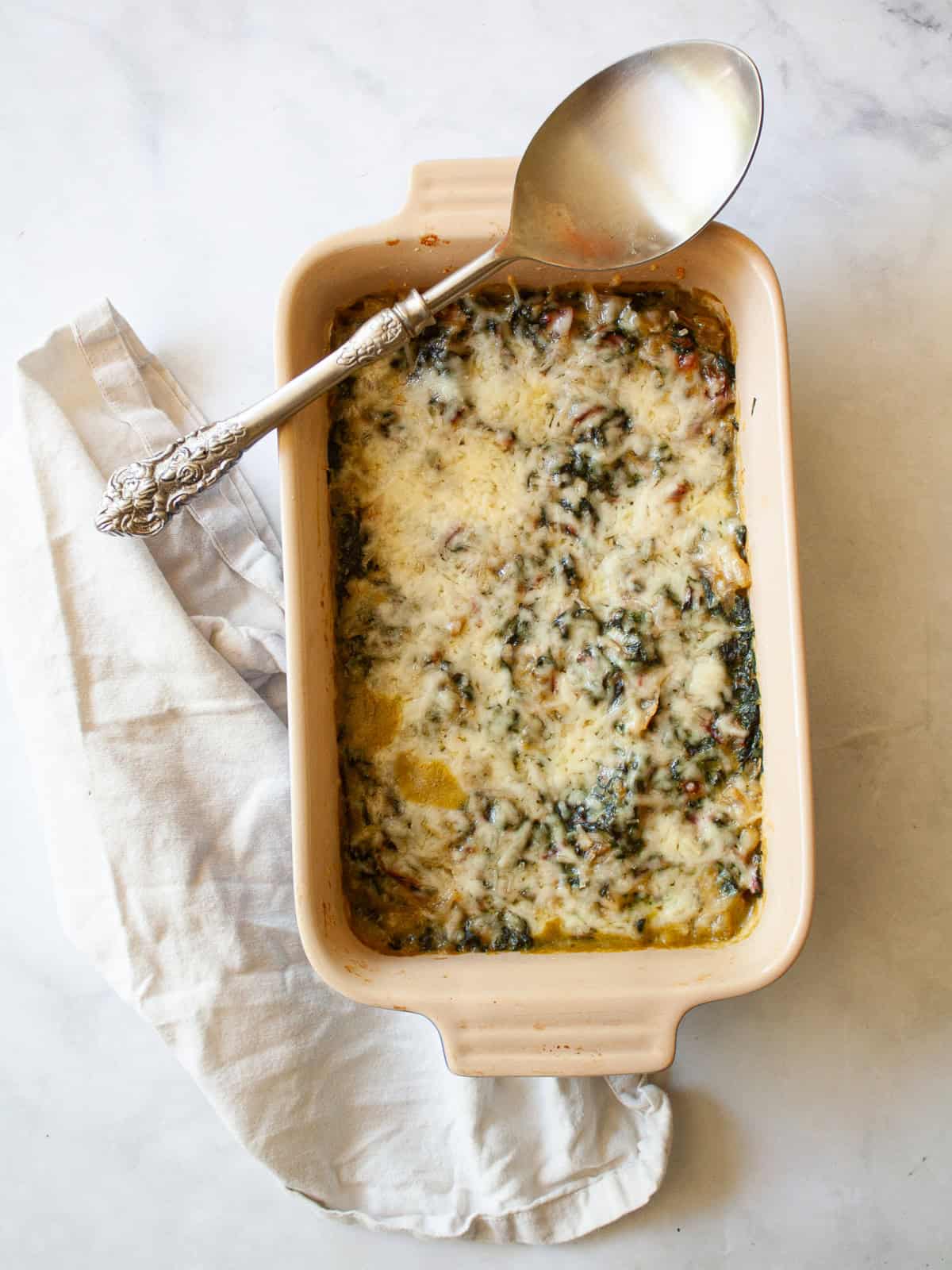 This easy chard gratin is a naturally gluten-free, vegetarian side dish made with fresh chard, onion, cheese, and milk. Perfect for fall and winter. A serving spoon rests on top of a dish of chard gratin.