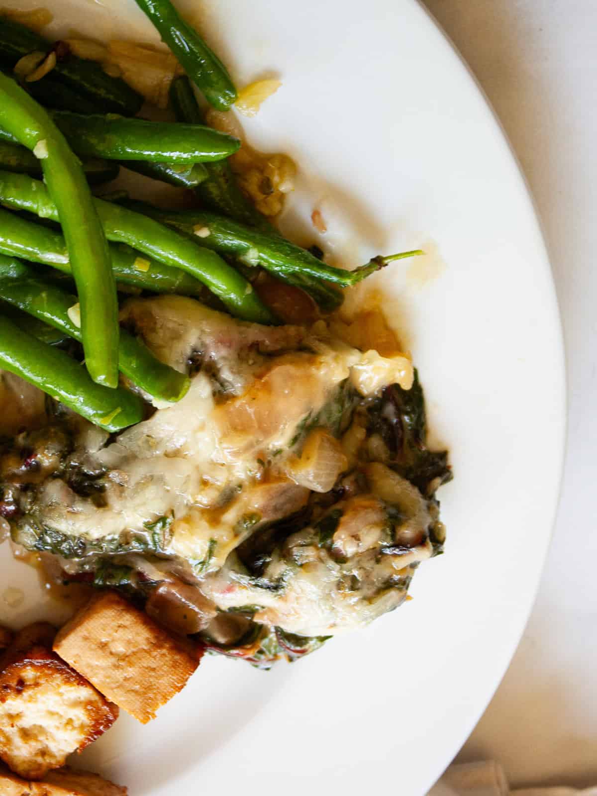 This easy chard gratin is a naturally gluten-free, vegetarian side dish made with fresh chard, onion, cheese, and milk. Perfect for fall and winter. A serving of chard gratin on a plate with green beans and tofu.