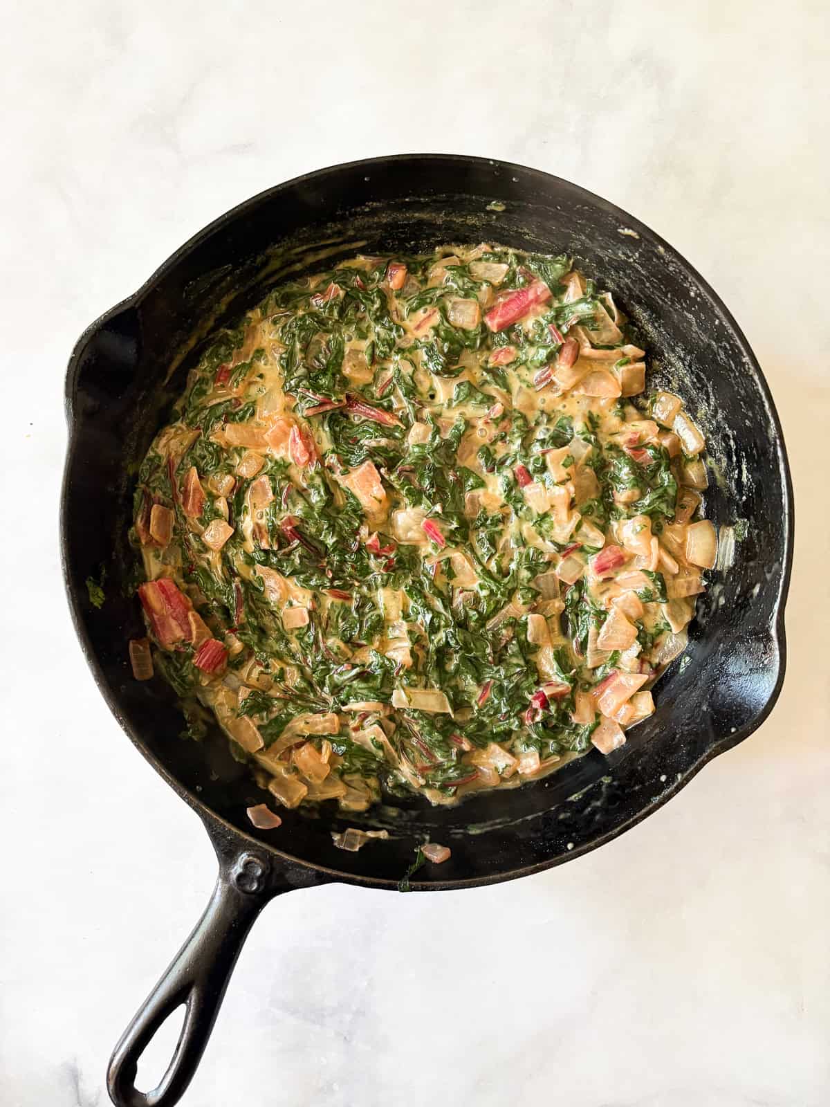 This easy chard gratin is a naturally gluten-free, vegetarian side dish made with fresh chard, onion, cheese, and milk. Perfect for fall and winter. Chard gratin in the pan.